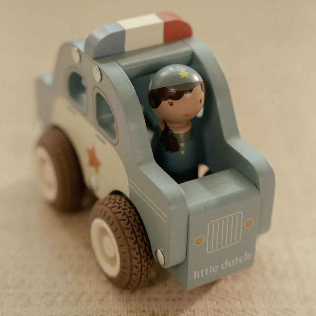 Toy police car with a figurine of a police officer on a beige background
