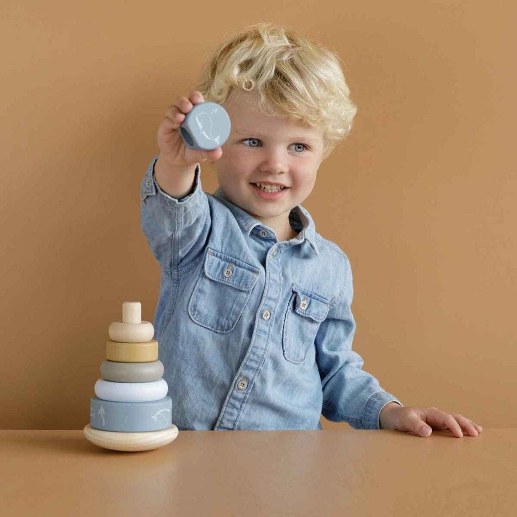 Boy holding up wooden piece of rocking ring stacker on a brown background.