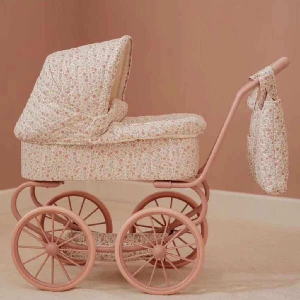 Vintage-style pink baby pram with floral pattern and a matching bag on a beige background