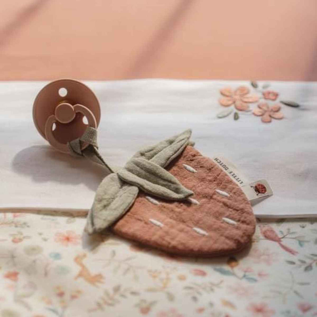 Baby pacifier with strawberry-shaped pacifier cloth on a floral blanket