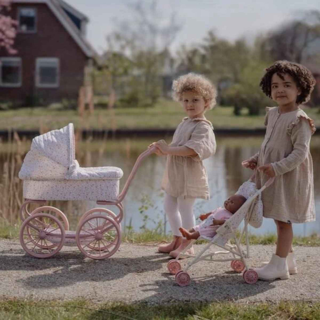 Two children playing with doll strollers by a lake.