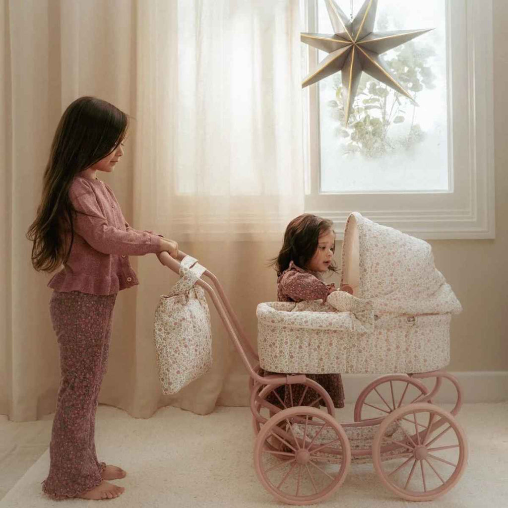 Two young girls playing with a vintage-style baby pram in a softly lit room.
