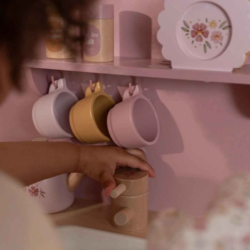 Child's hand reaching for a wooden tap on a pink kitchen shelf with colorful mugs.