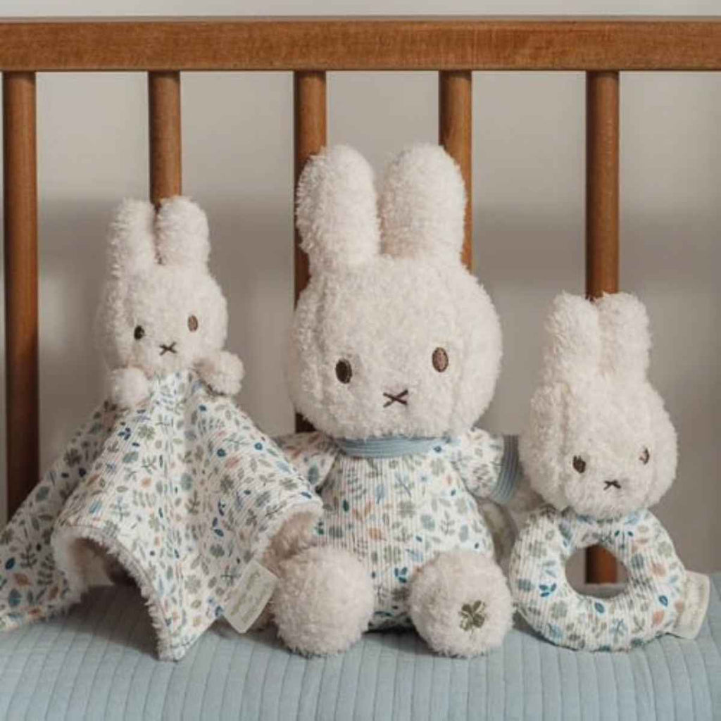 Three plush bunny toys with blankets and a rattle on a crib